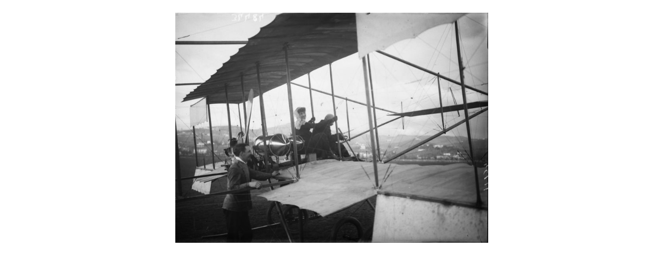 Mario Nunes Vais, Biplano e aviatori ripresi prima della partenza, a Campo di Marte, in occasione della I Dimostrazione di volo - una signora salita a bordo del velivolo, si gira sorridente verso l'obiettivo, 1910, gelatina ai sali d'argento, F034484